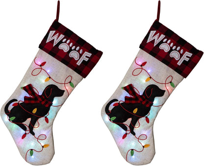 Pair of Glitzhome LED dog Christmas stockings – cream linen with black dog silhouette, red plaid "WOOF" cuff, and light-up embroidered string lights