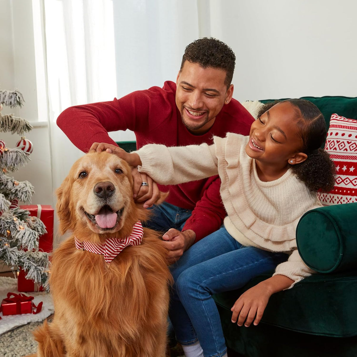 Happy family petting a golden retriever in a holiday scarf beside a Christmas tree